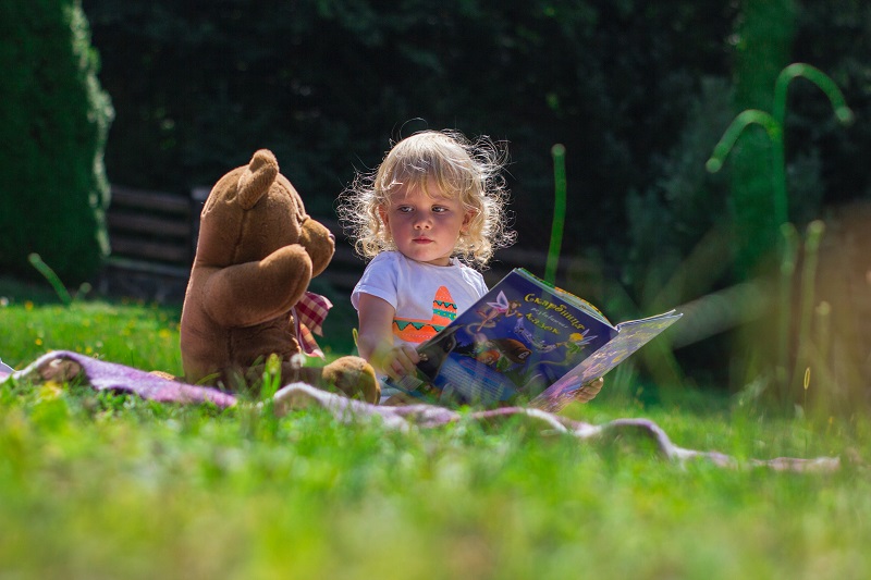 Balance Bike Tips for Toddlers a Toddler Reading a Book to a Teddy Bear in a Field