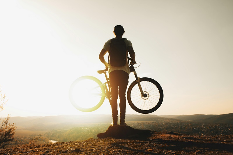 Best Bike Trails in Minnesota a Person Standing on a Cliff Holding a Bike Looking at the Sun Rising