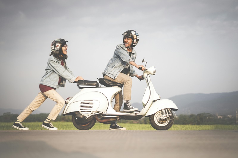 Types of Helmets for Kids a Man Riding a Vespa with a Person Standing Behind it Both Wearing Open-Face Helmets